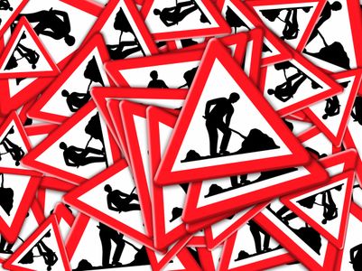 Verschiedene Baustellenschilder in rotem und schwarzem Design, die Bauarbeiten symbolisieren, übereinander gestapelt.